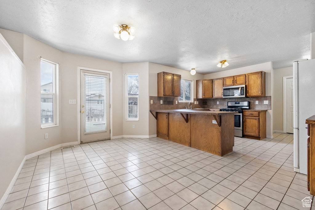 Kitchen featuring a kitchen bar, appliances with stainless steel finishes, backsplash, light tile patterned floors, and kitchen peninsula