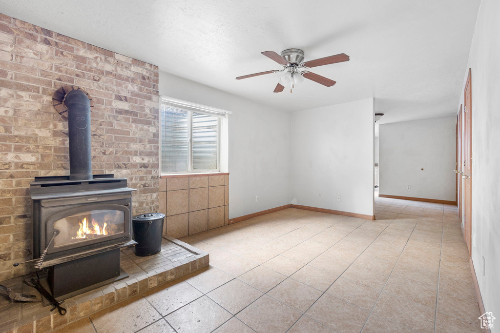 Unfurnished living room with ceiling fan, light tile patterned floors, and a wood stove