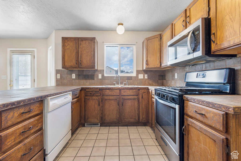 Kitchen with kitchen peninsula, sink, backsplash, light tile patterned floors, and appliances with stainless steel finishes