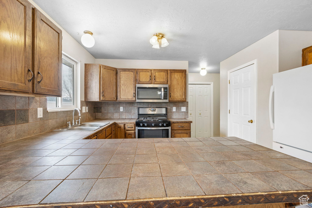 Kitchen featuring sink, backsplash, appliances with stainless steel finishes, and tile countertops