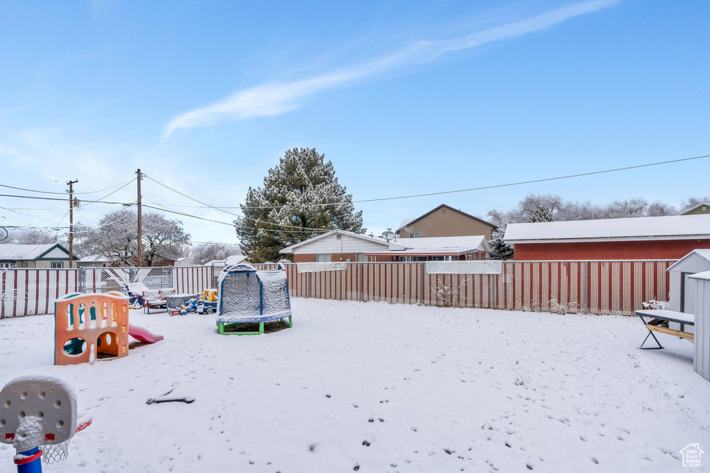 Yard layered in snow featuring a playground and a trampoline