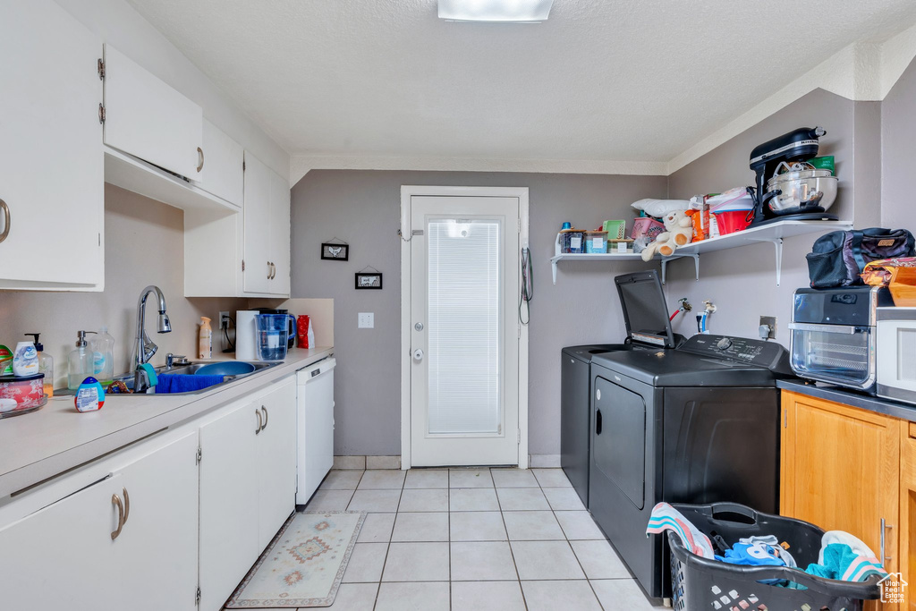 Kitchen featuring washer and dryer, dishwasher, sink, white cabinets, and light tile patterned floors