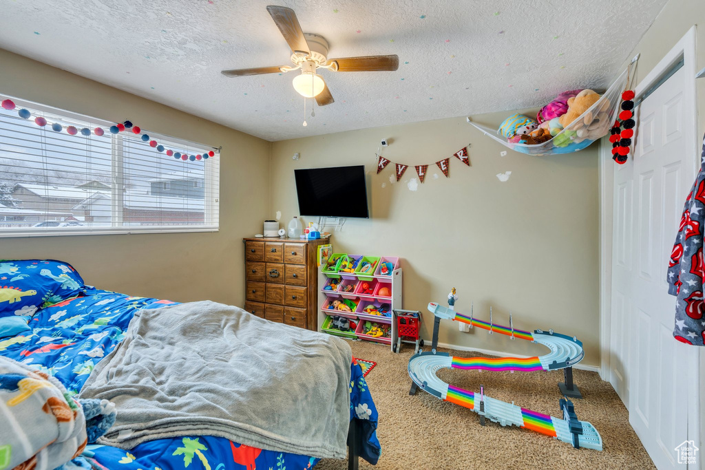 Carpeted bedroom with ceiling fan and a textured ceiling