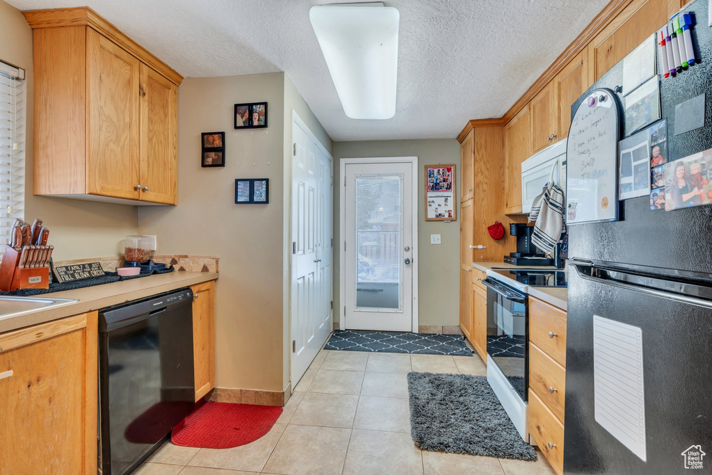 Kitchen with a textured ceiling, light tile patterned floors, fridge, range with electric stovetop, and black dishwasher