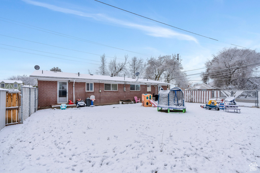 Snow covered rear of property featuring a playground and a trampoline