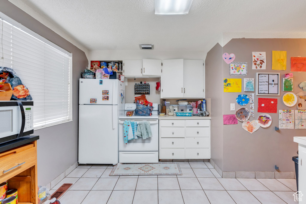 Kitchen featuring white cabinetry, light tile patterned floors, a textured ceiling, and white appliances