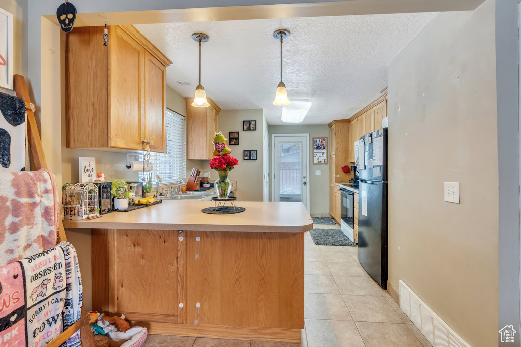 Kitchen with black refrigerator, kitchen peninsula, sink, and pendant lighting