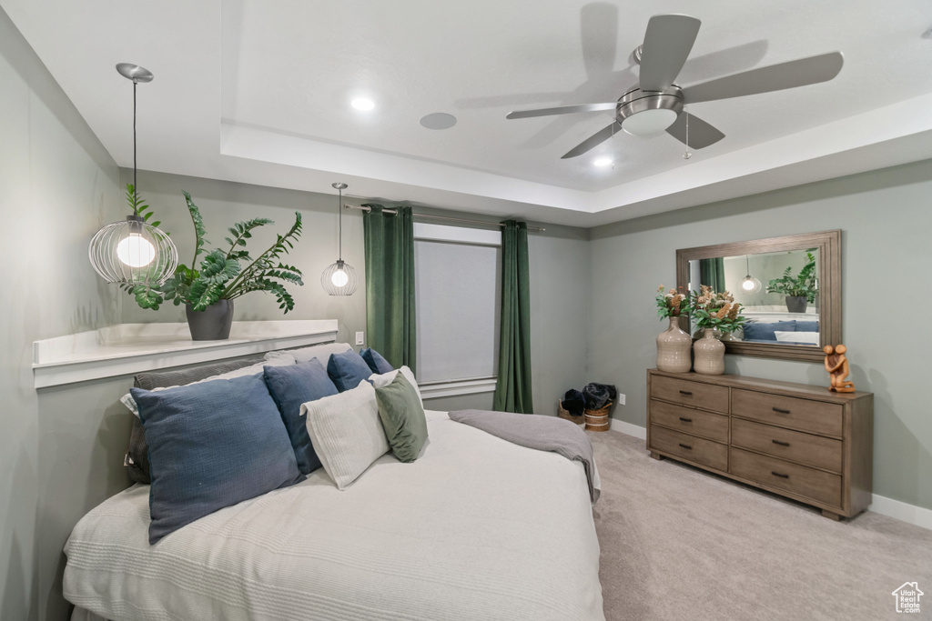 Bedroom with a raised ceiling, light carpet, and ceiling fan