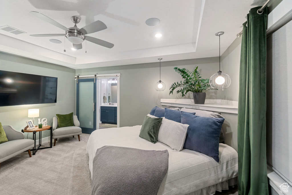 Carpeted bedroom with a tray ceiling, a barn door, ceiling fan, and ensuite bathroom