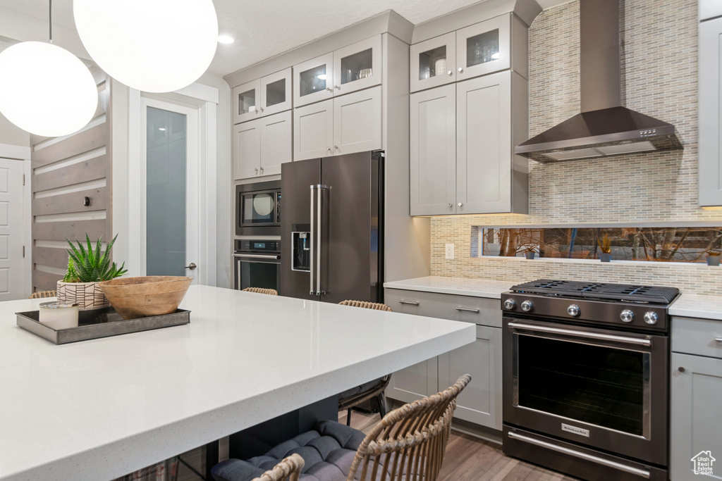 Kitchen featuring appliances with stainless steel finishes, gray cabinetry, wall chimney range hood, pendant lighting, and backsplash