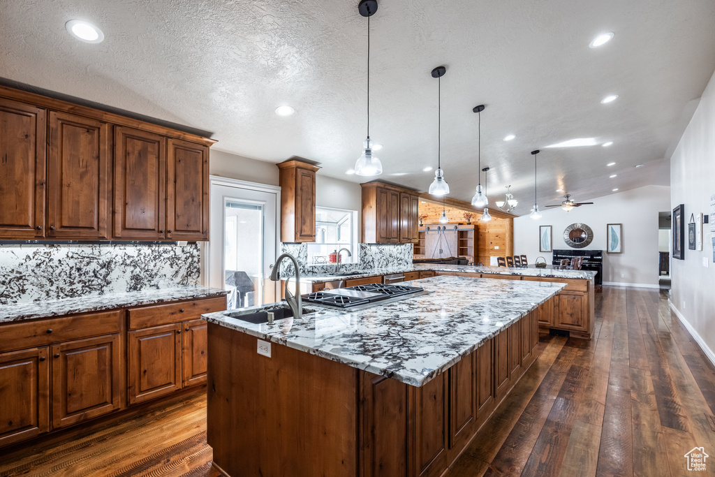 Kitchen featuring a sink, a kitchen island with sink, a peninsula, backsplash, and dark wood finished floors