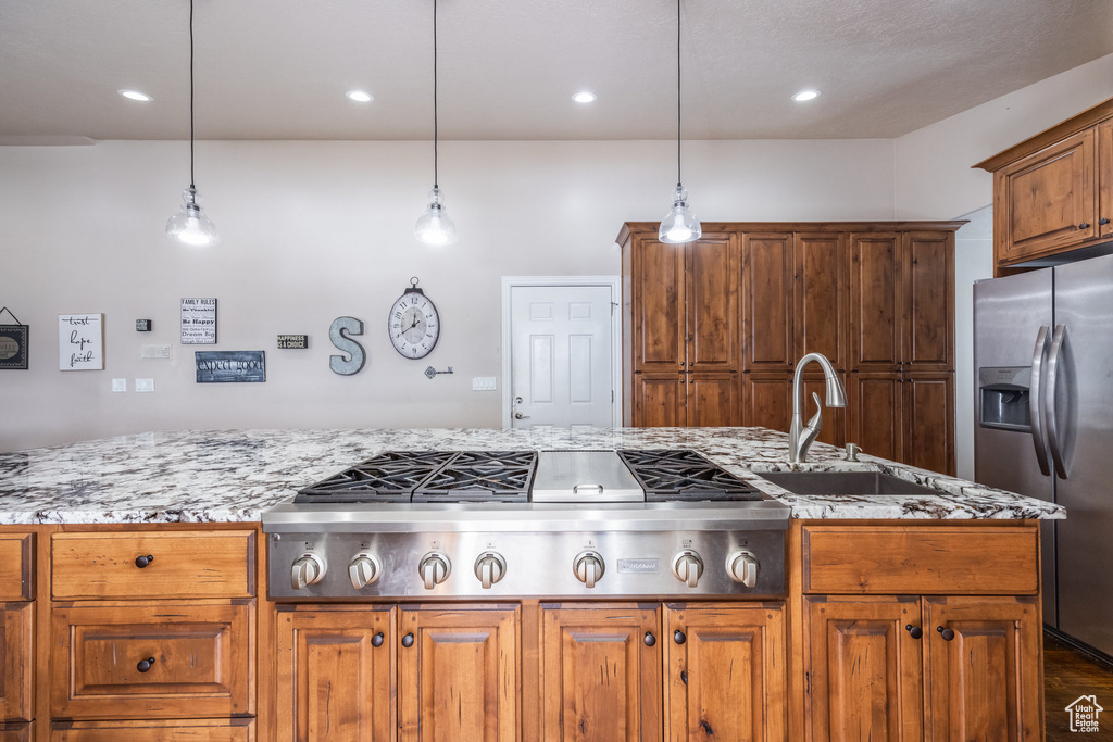 Kitchen with appliances with stainless steel finishes, a sink, light stone countertops, brown cabinetry, and recessed lighting
