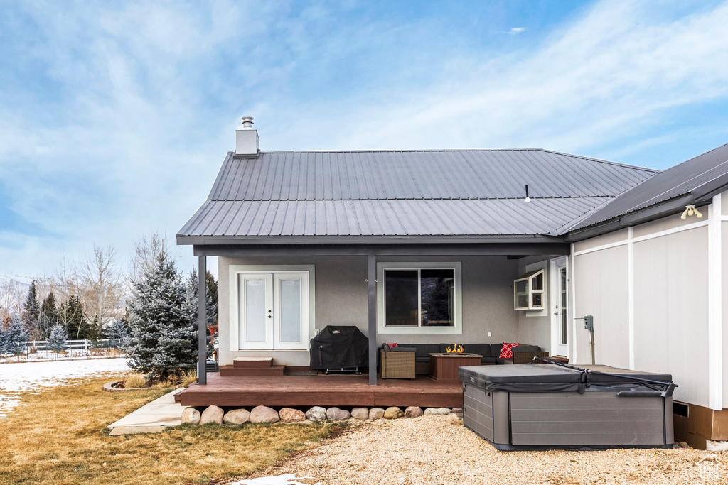 Rear view of property featuring a hot tub, a wooden deck, metal roof, and a chimney