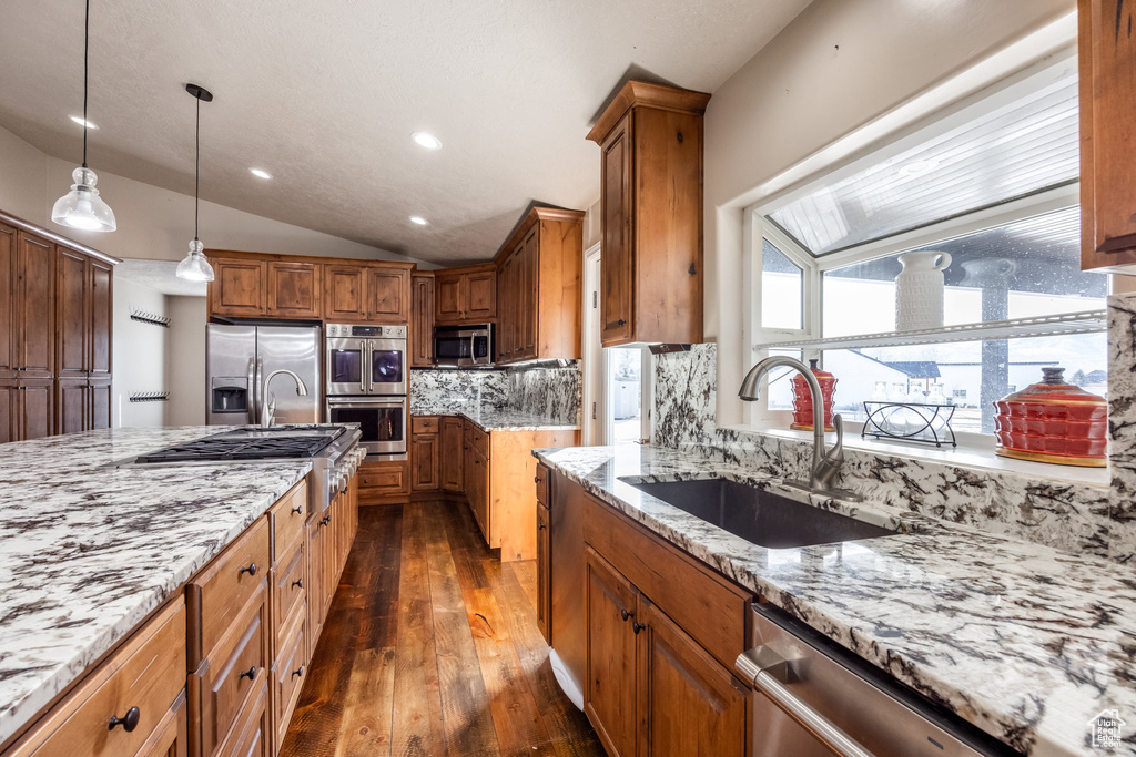 Kitchen featuring stainless steel appliances, a sink, dark wood-type flooring, light stone countertops, and vaulted ceiling