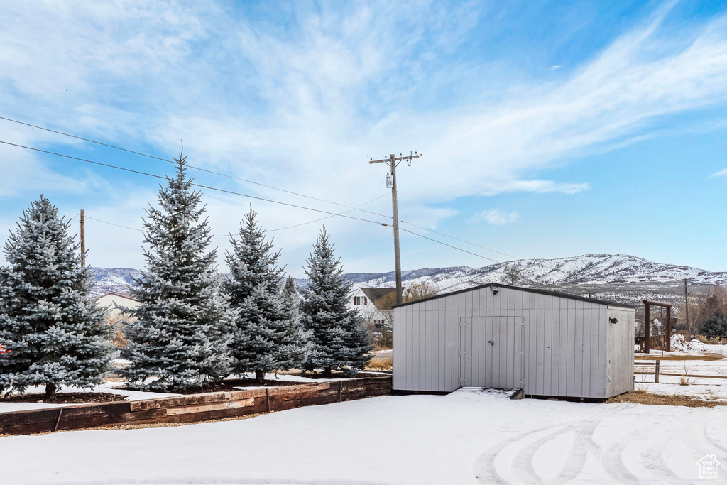 Snow covered structure featuring a shed, an outdoor structure, a mountain view, and fence
