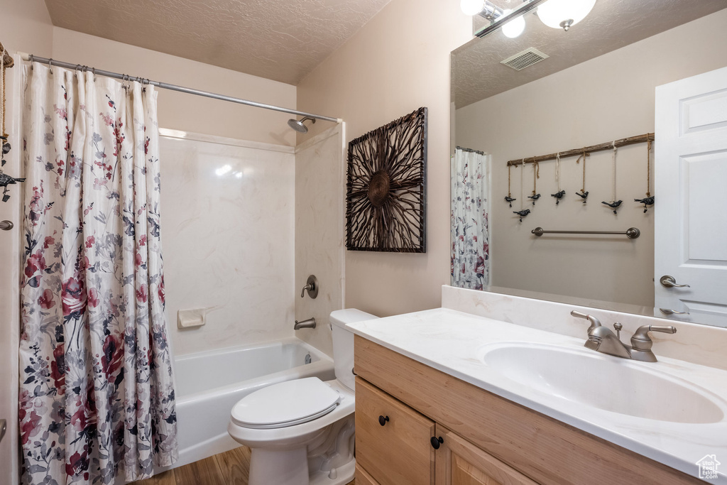 Full bath featuring a textured ceiling, toilet, vanity, shower / bath combo, and wood finished floors