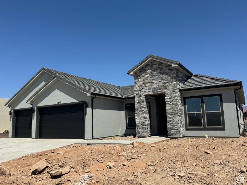View of front of home with an attached garage, stucco siding, driveway, and a tile roof