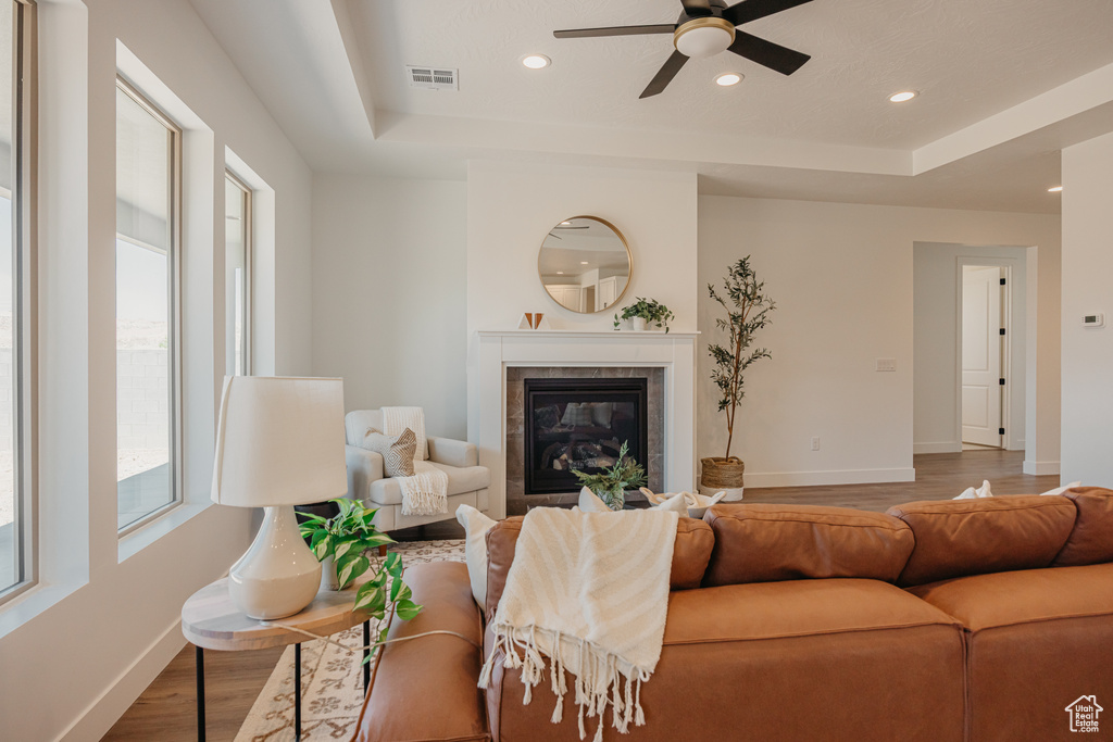 Living area featuring wood finished floors, ceiling fan, a raised ceiling, recessed lighting, and a tiled fireplace