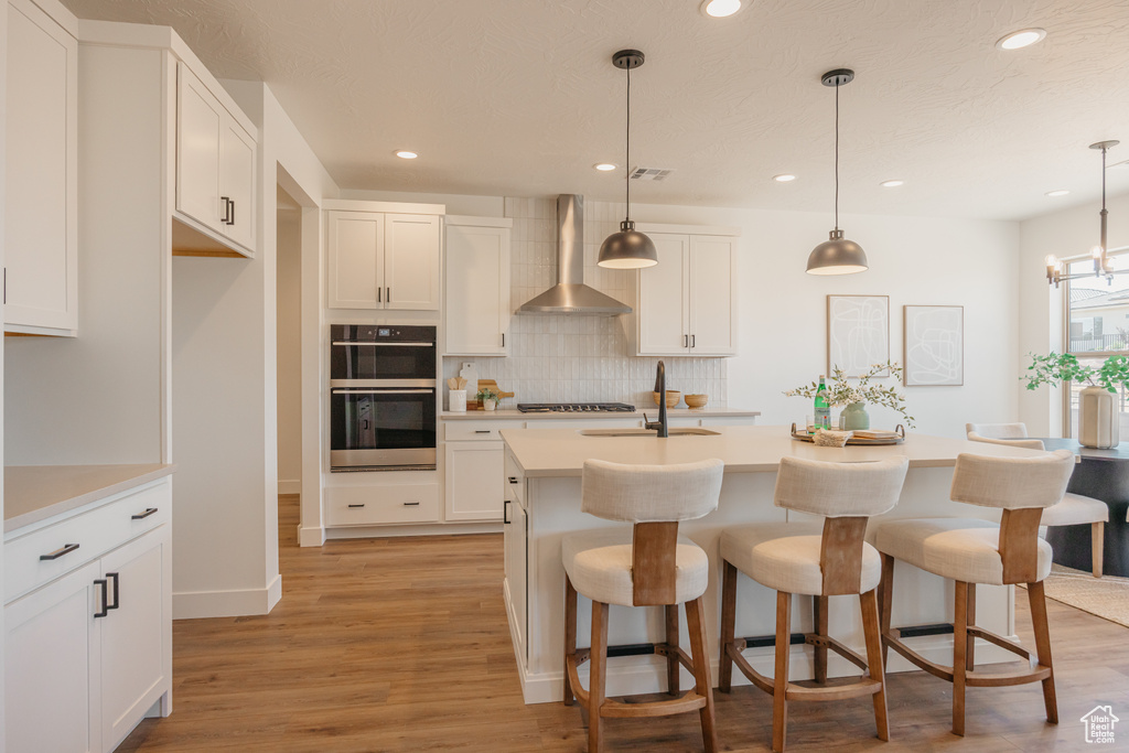 Kitchen featuring wall chimney exhaust hood, stainless steel appliances, decorative backsplash, recessed lighting, and light wood finished floors