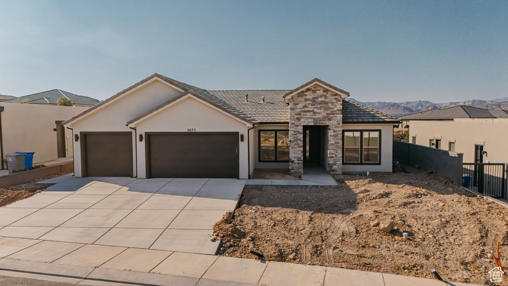 View of front of house with an attached garage, driveway, stucco siding, and stone siding