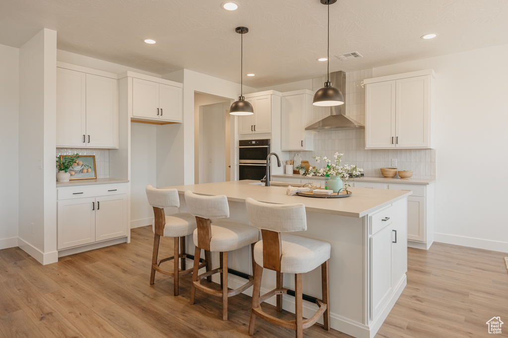Kitchen featuring wall chimney exhaust hood, light wood-type flooring, decorative backsplash, white cabinets, and recessed lighting