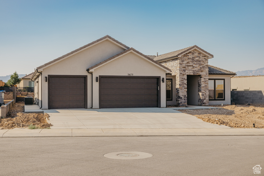 View of front of house with an attached garage, stucco siding, driveway, stone siding, and a tile roof