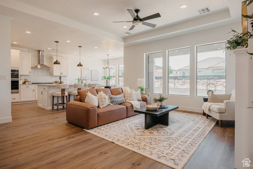 Living room featuring a tray ceiling, a ceiling fan, light wood-style flooring, and recessed lighting