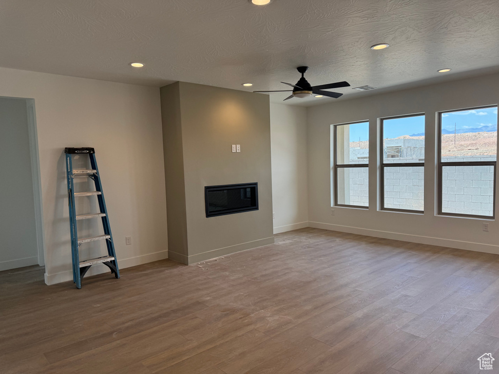 Unfurnished living room with a glass covered fireplace, a ceiling fan, wood finished floors, a textured ceiling, and baseboards