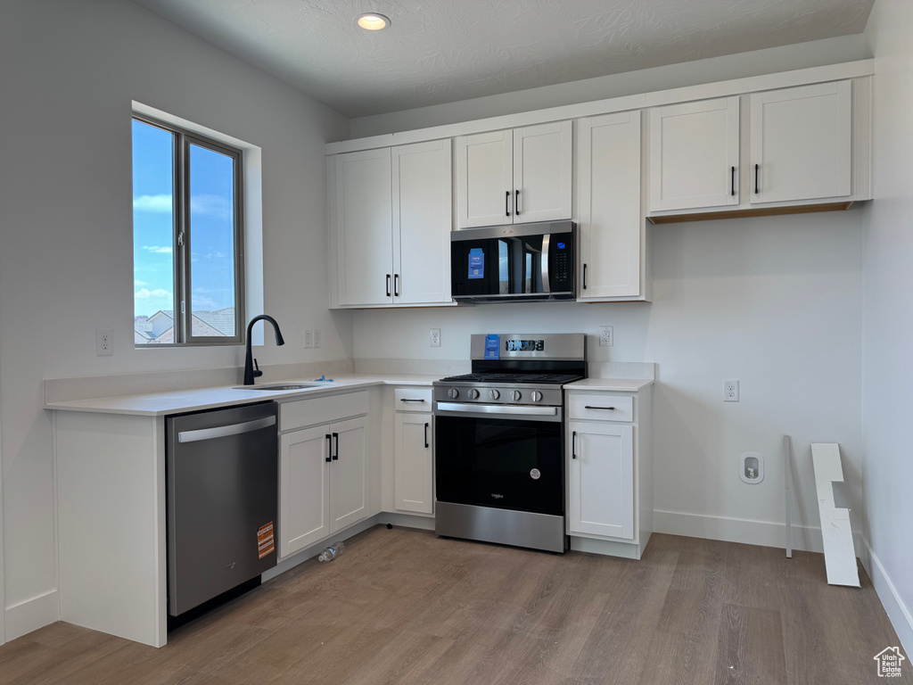 Kitchen with appliances with stainless steel finishes, a sink, light wood finished floors, white cabinetry, and recessed lighting