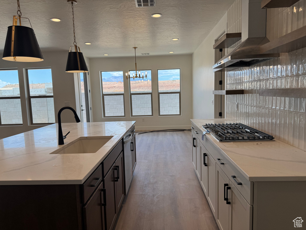 Kitchen featuring stainless steel gas stovetop, a sink, a center island with sink, a chandelier, and light wood finished floors