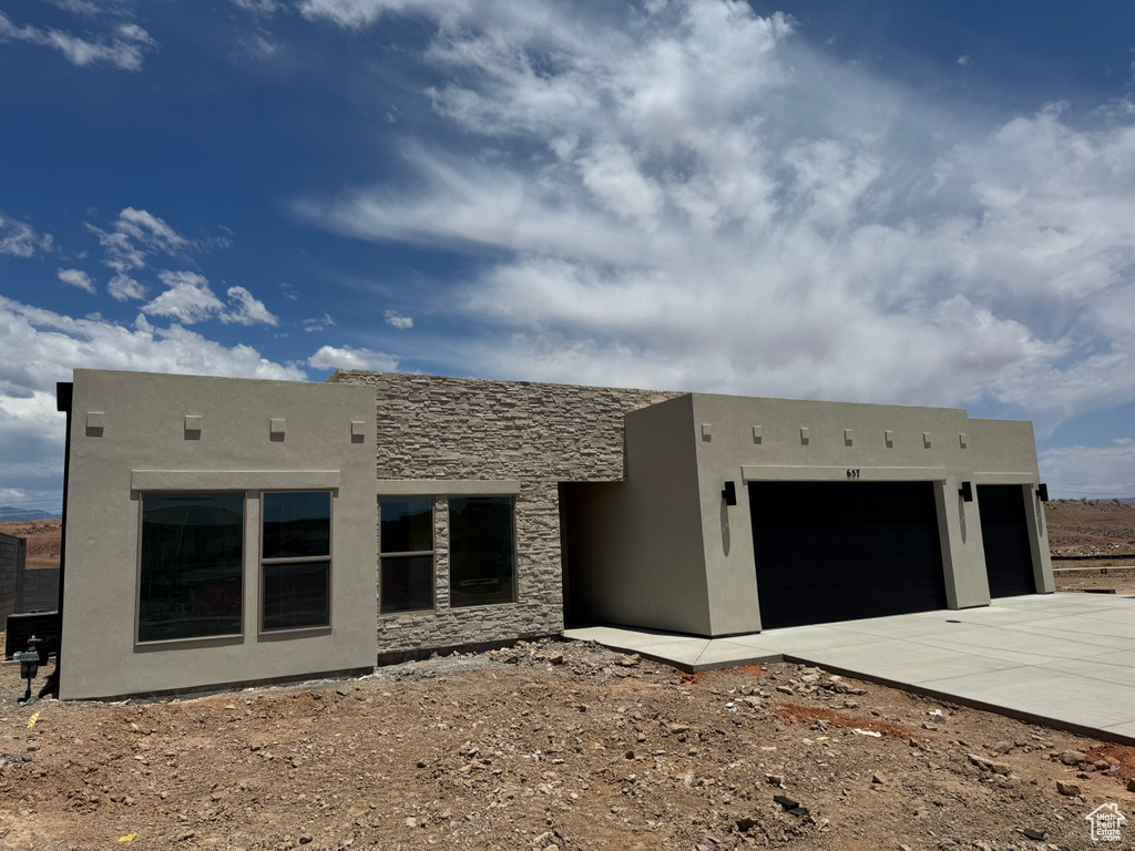 Southwest-style home with an attached garage, concrete driveway, stucco siding, and stone siding