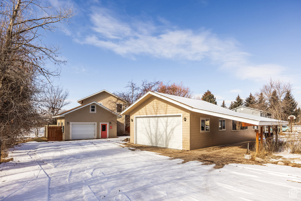 View of snowy exterior with an outdoor structure and a garage