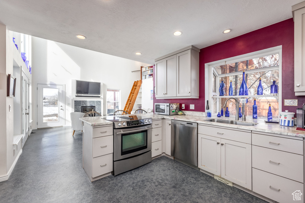 Kitchen featuring appliances with stainless steel finishes, a sink, a peninsula, recessed lighting, and a tiled fireplace