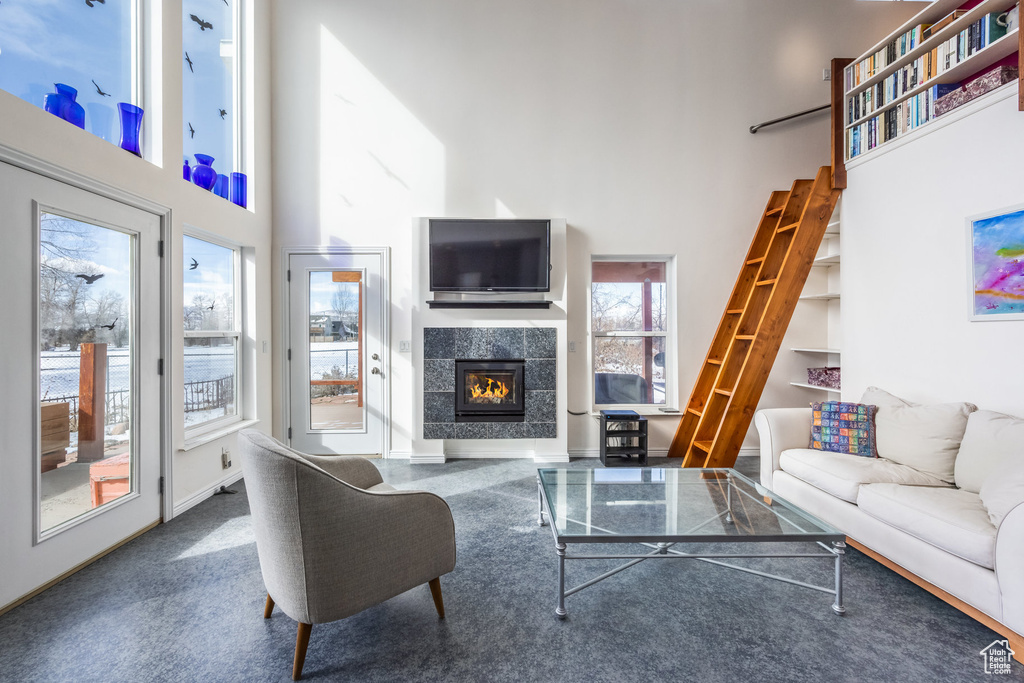 Living area with a high ceiling, healthy amount of natural light, a tiled fireplace, baseboards, and stairs