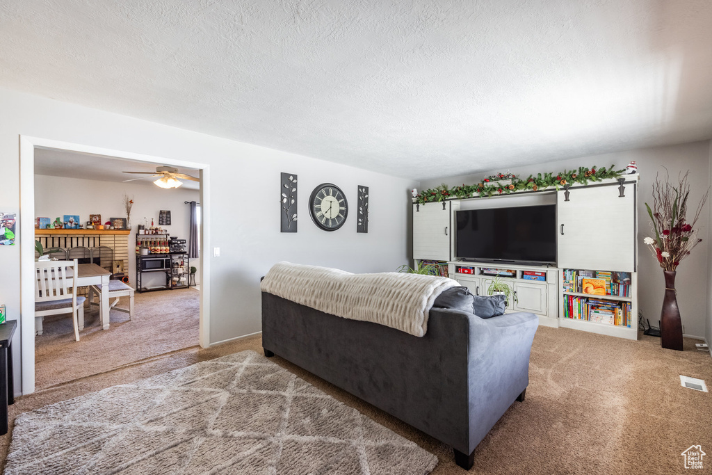 Carpeted living area with a brick fireplace, ceiling fan, and a textured ceiling