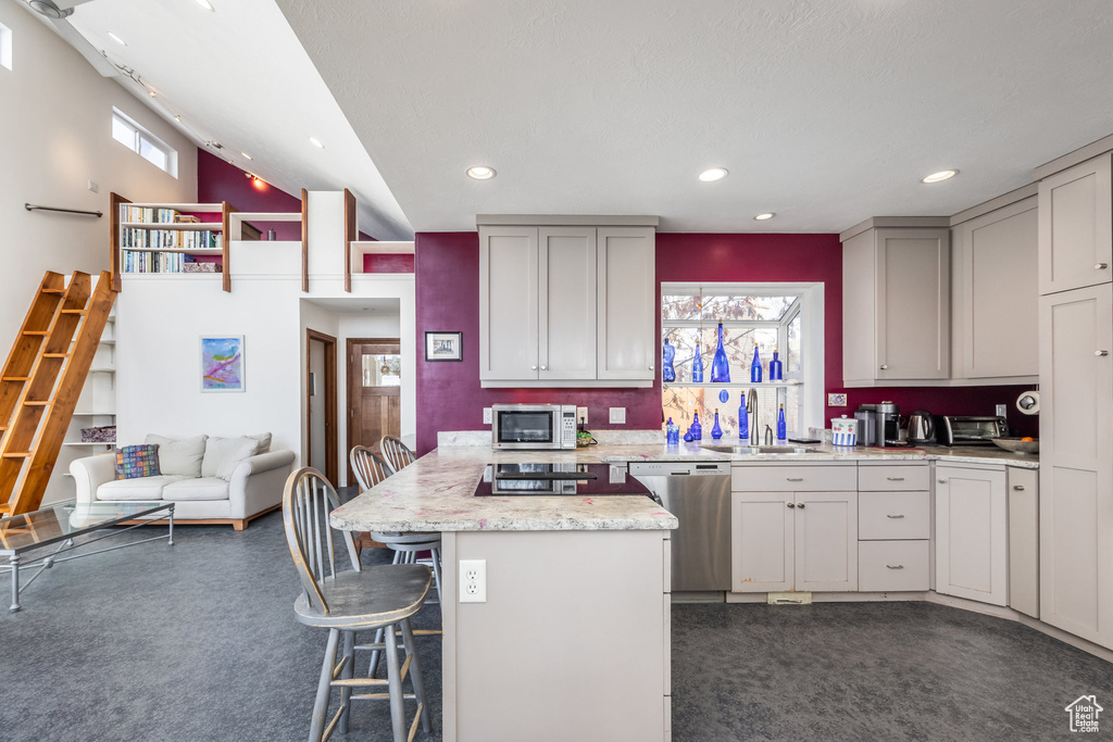 Kitchen featuring appliances with stainless steel finishes, dark colored carpet, a kitchen bar, a peninsula, and recessed lighting