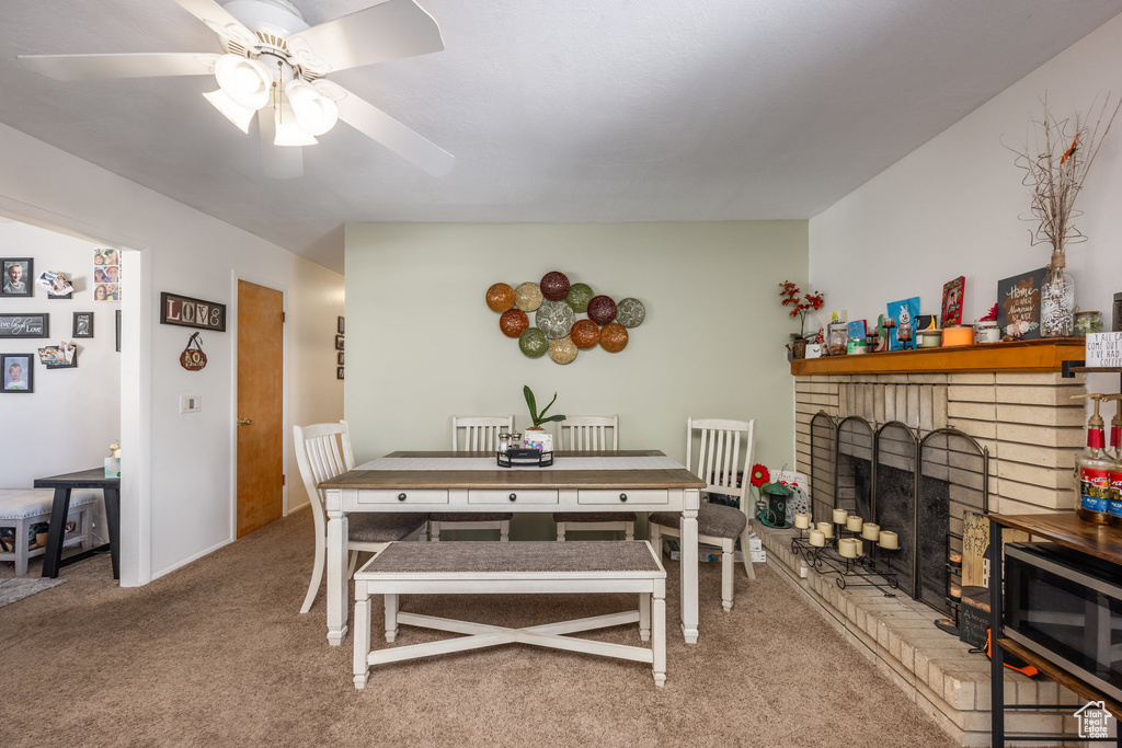 Dining space with a ceiling fan, light carpet, and a brick fireplace