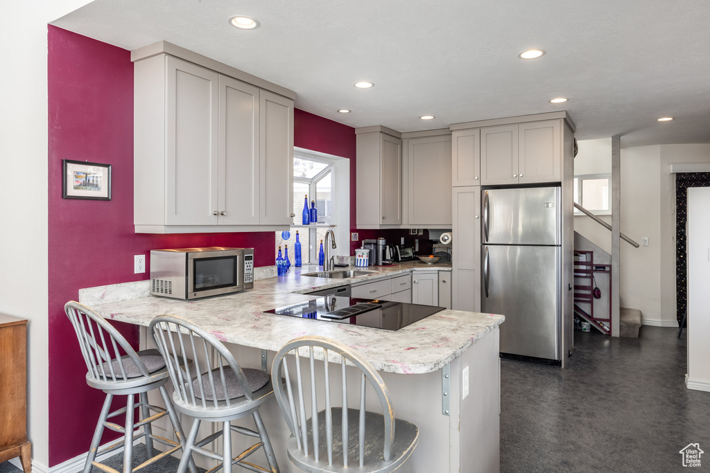 Kitchen featuring appliances with stainless steel finishes, a sink, gray cabinets, baseboards, and a peninsula