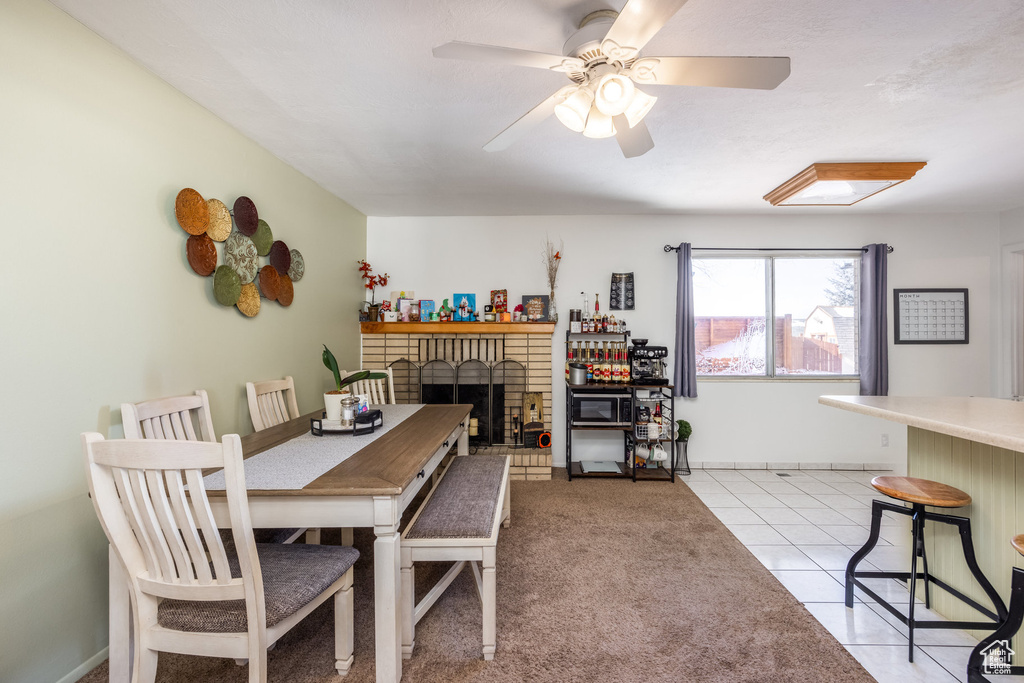 Dining area featuring a brick fireplace, light tile patterned floors, and a ceiling fan