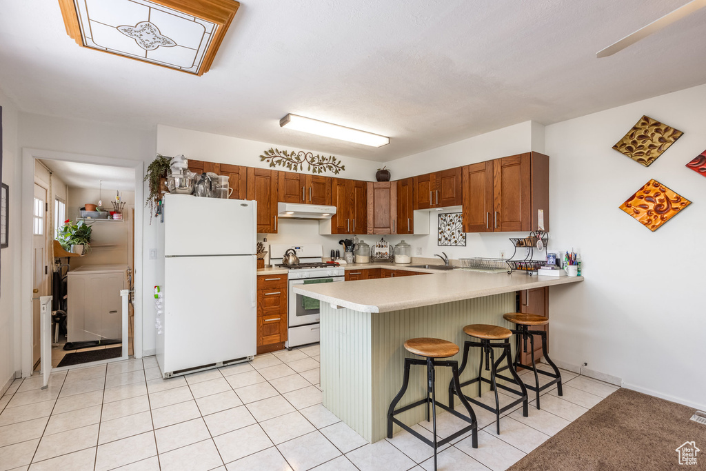 Kitchen with white appliances, a peninsula, under cabinet range hood, light countertops, and a breakfast bar area