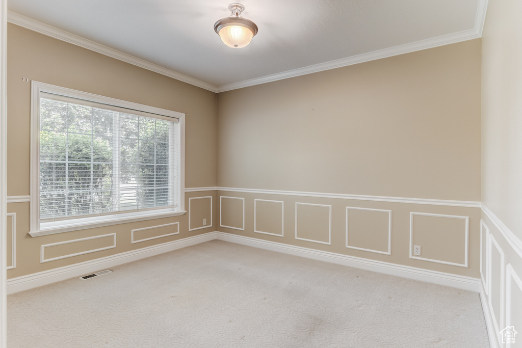 Unfurnished room with light colored carpet, ornamental molding, a wainscoted wall, and a decorative wall