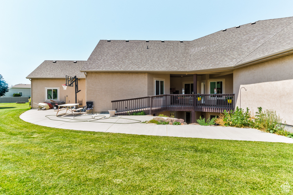 Back of house with a patio, stucco siding, a lawn, roof with shingles, and a wooden deck