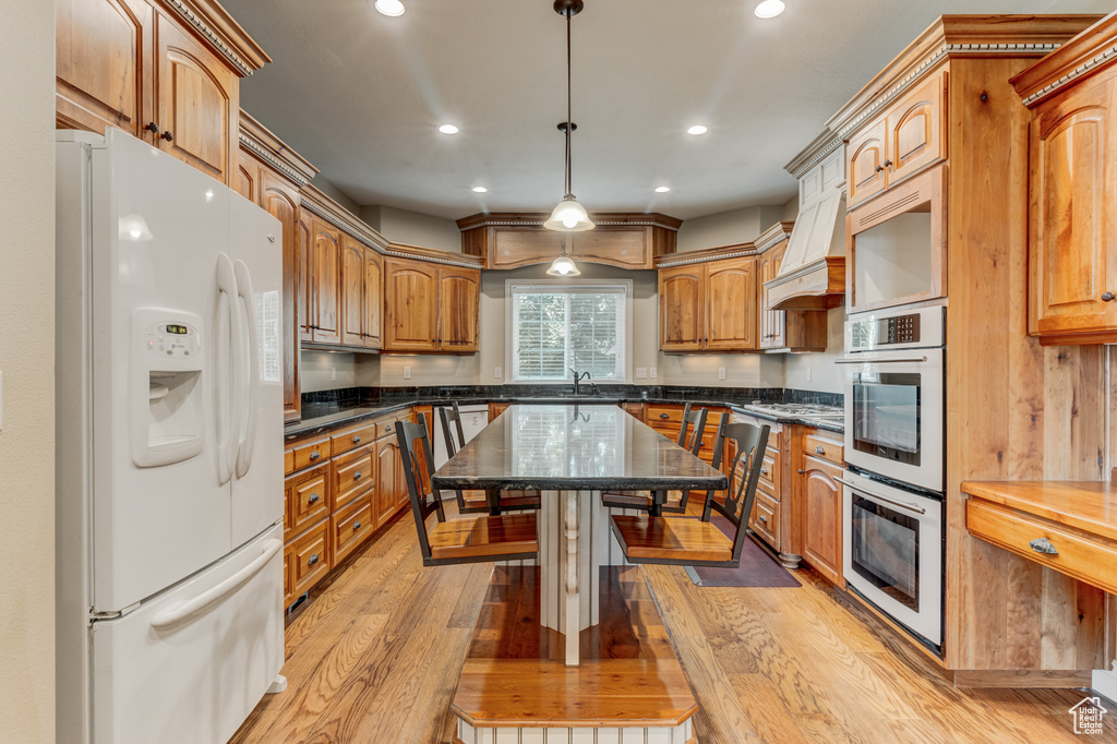 Kitchen featuring white refrigerator with ice dispenser, recessed lighting, stainless steel double oven, light wood-style flooring, and pendant lighting