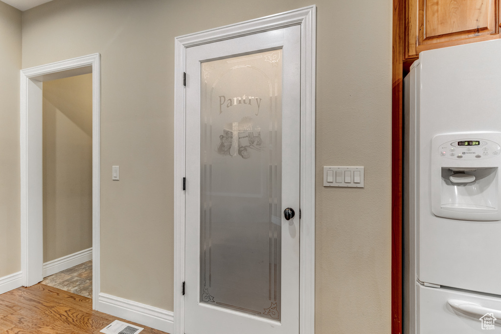 Detailed view of white fridge with ice dispenser and light wood-style floors