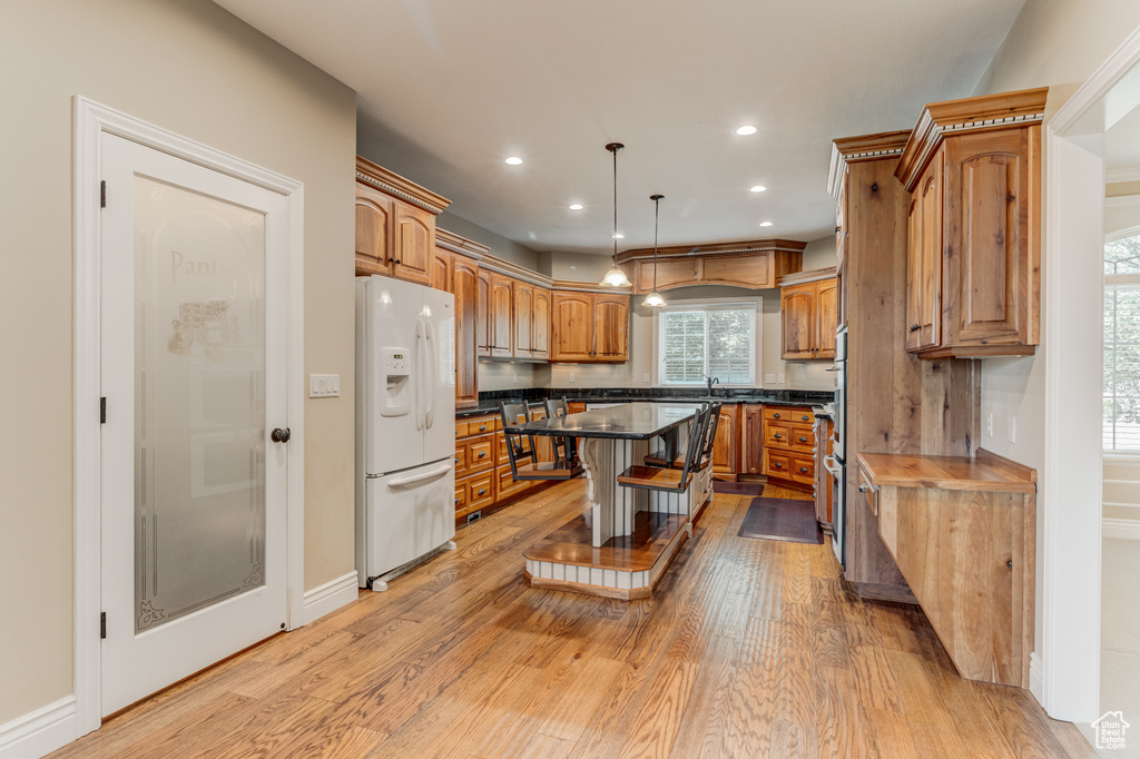 Kitchen featuring white refrigerator with ice dispenser, brown cabinetry, light wood-type flooring, dark countertops, and recessed lighting
