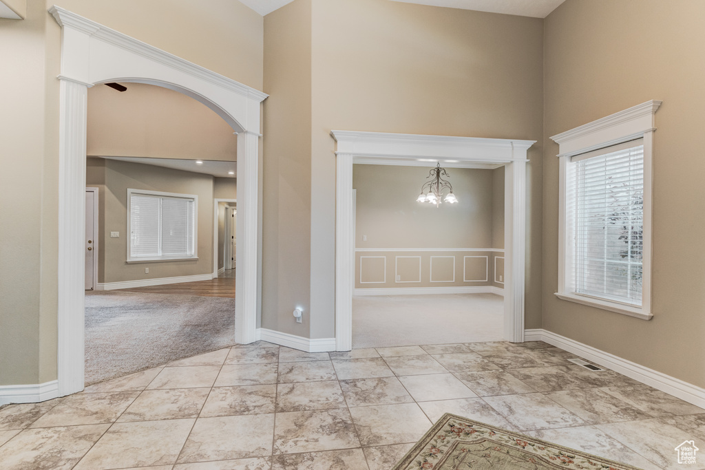 Spare room with a towering ceiling, light carpet, a chandelier, and arched walkways