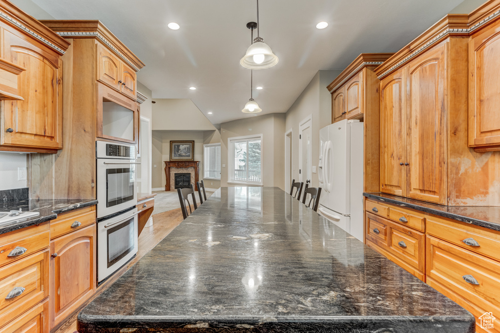 Kitchen with white fridge with ice dispenser, double wall oven, a kitchen island, decorative light fixtures, and recessed lighting