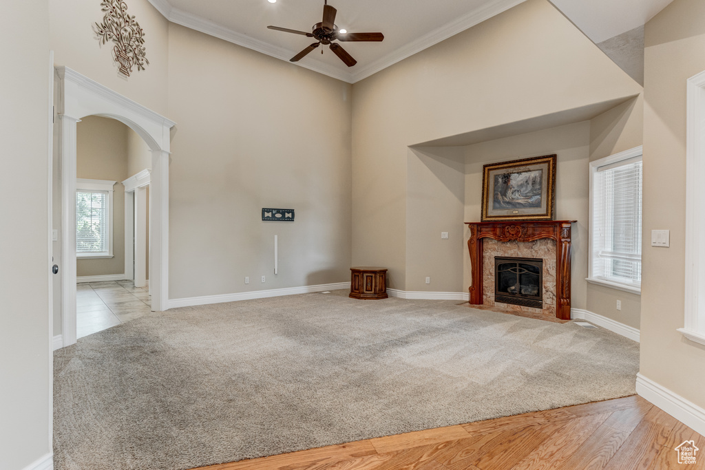 Unfurnished living room with a ceiling fan, a high ceiling, a high end fireplace, arched walkways, and ornamental molding