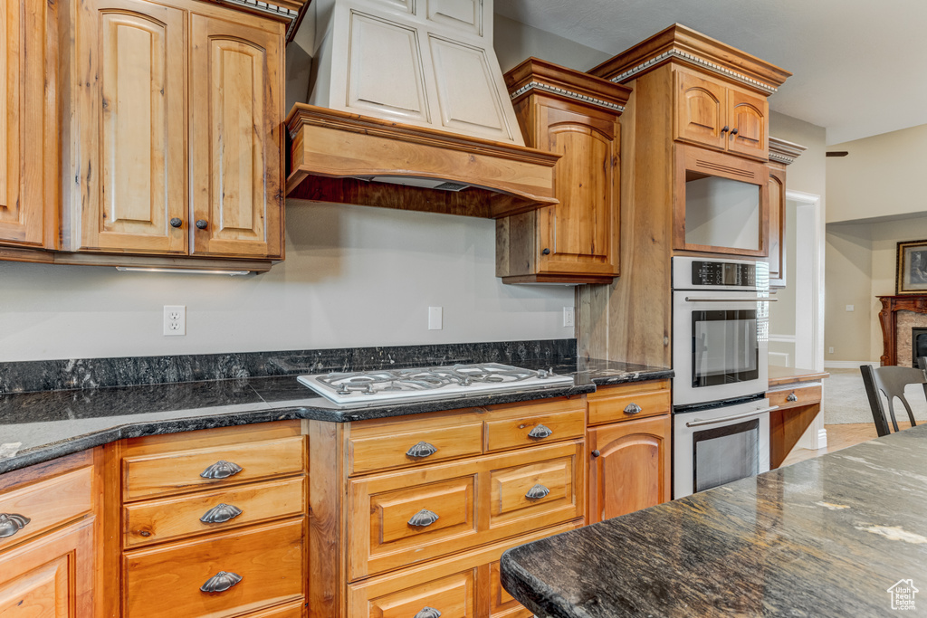 Kitchen featuring custom exhaust hood, double oven, white gas stovetop, a fireplace, and brown cabinets