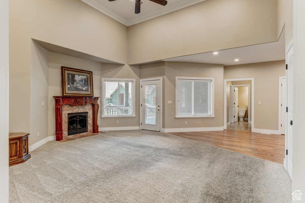 Unfurnished living room with a ceiling fan, carpet, a high ceiling, a fireplace, and crown molding
